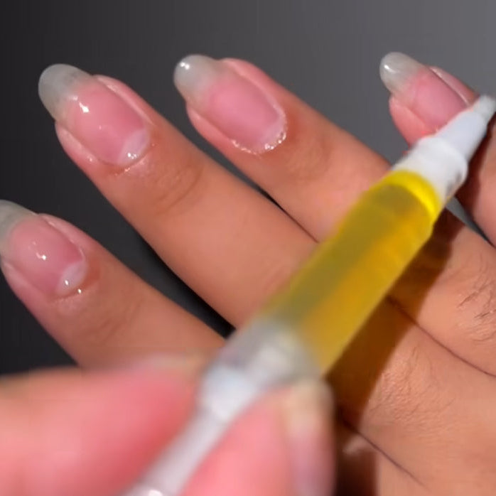 Hand holding a small bottle with a yellow liquid against a dark background